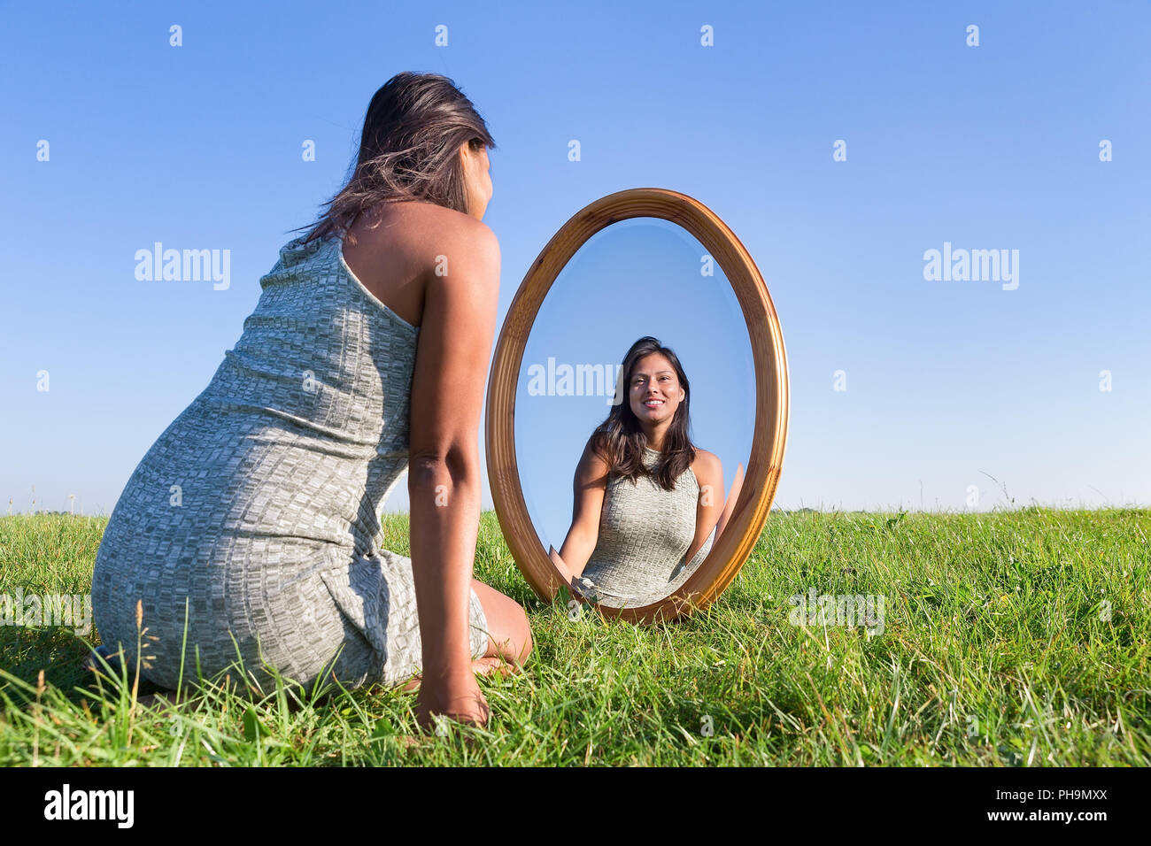 Woman kneeling on grass looking at mirror image Stock Photo