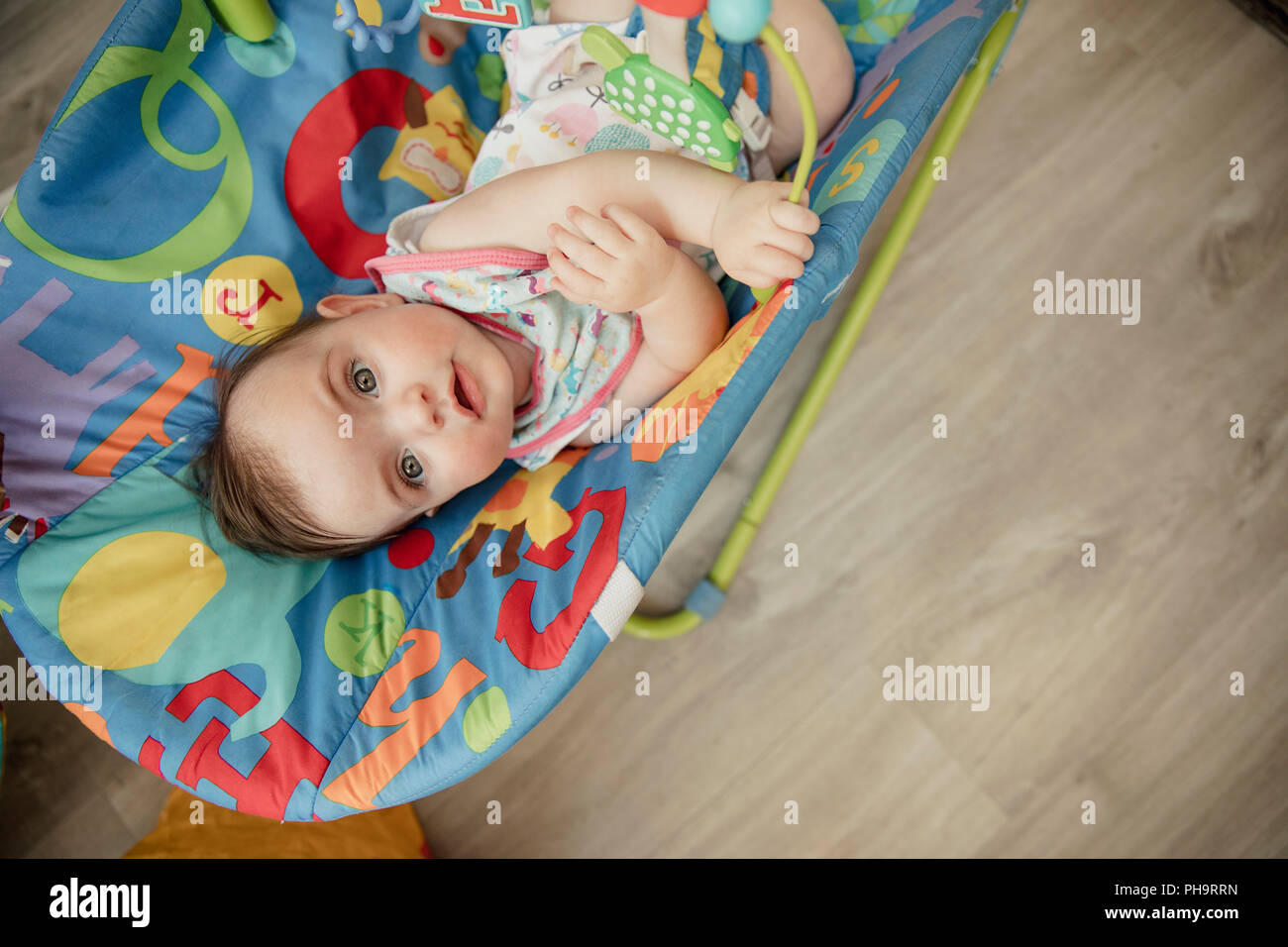 High angle view looking down onto a baby girl relaxing in her baby bouncer. The baby is looking up into the camera and smiling. Stock Photo