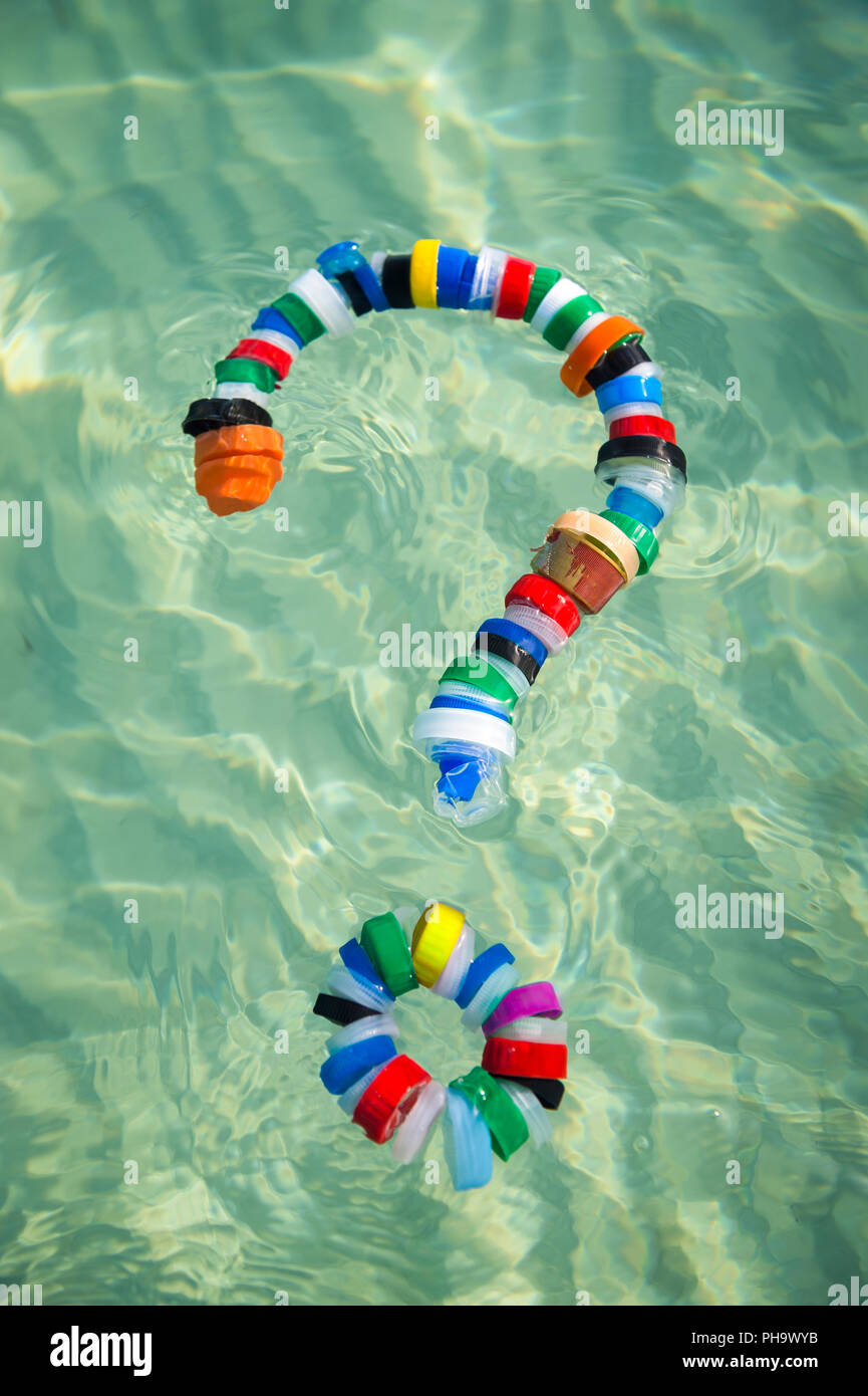 Colorful bottle caps in the shape of a question mark floating on the sea. Question plastic use and pollution it causes. Reduce, reuse and recycle. Stock Photo
