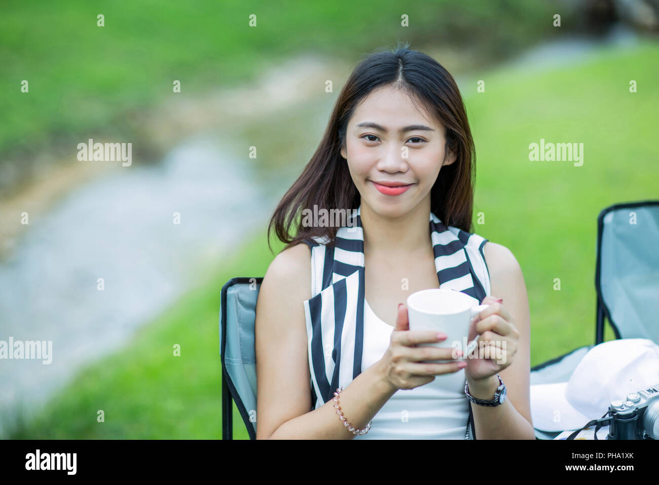 Asian girl holding a cup of coffee near the stream in the garden Stock Photo