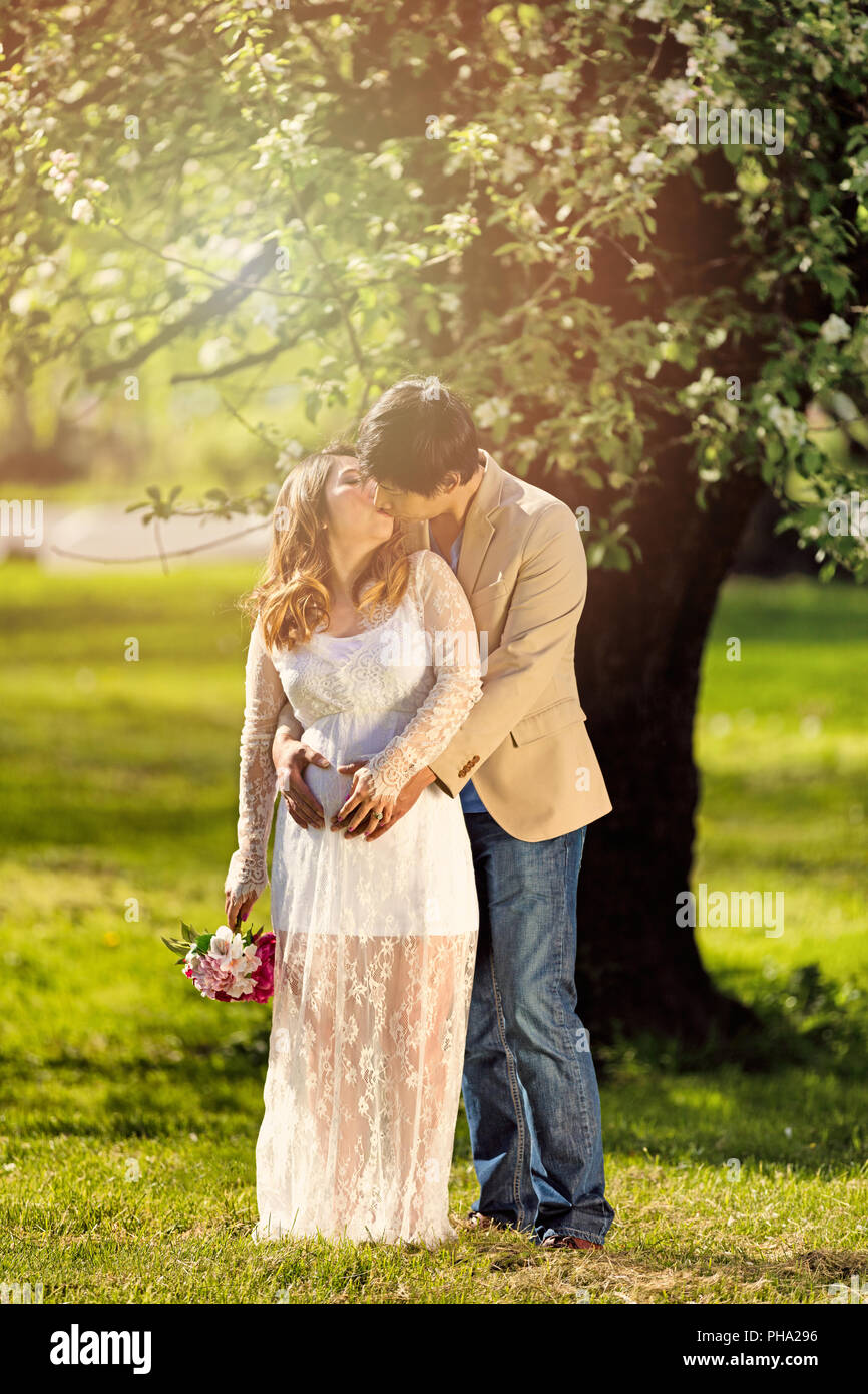 Expecting mom and dad kissing under flowering tree Stock Photo