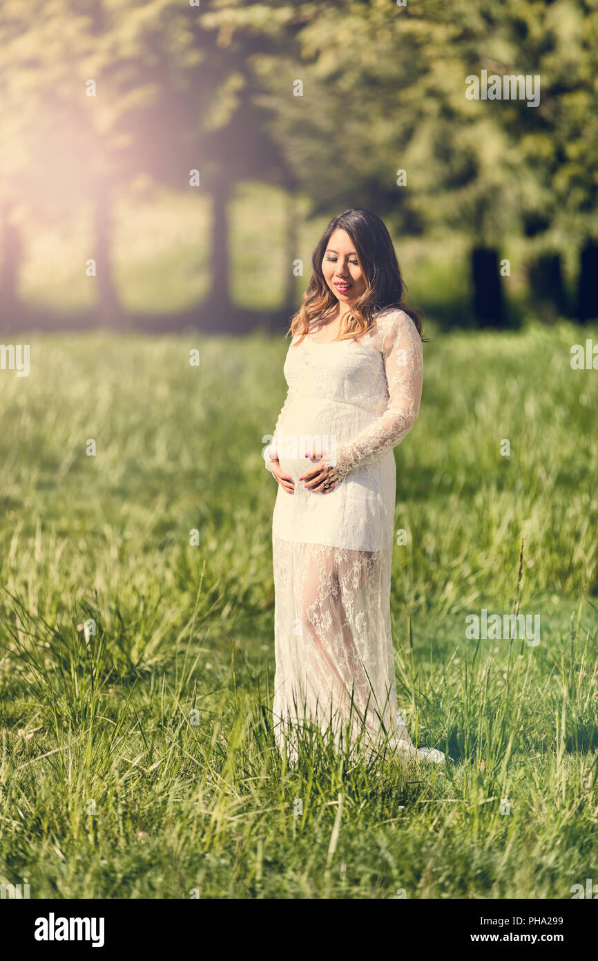 Expecting mom touching her abdomen while outdoors on sunny day Stock Photo