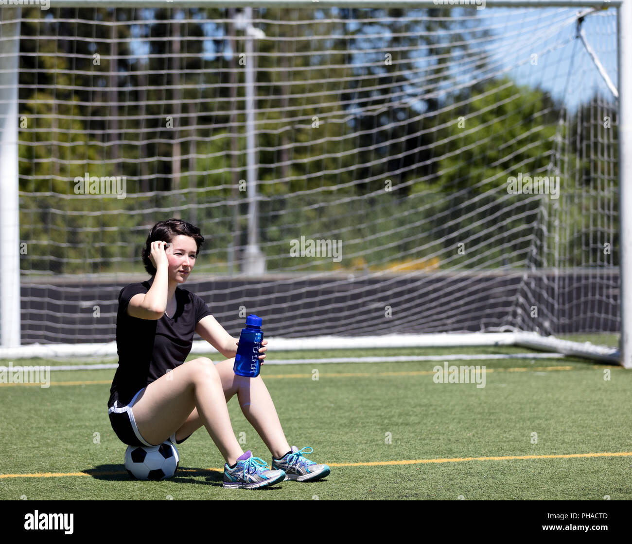 Teen girl resting on soccer ball while holding water bottle Stock Photo