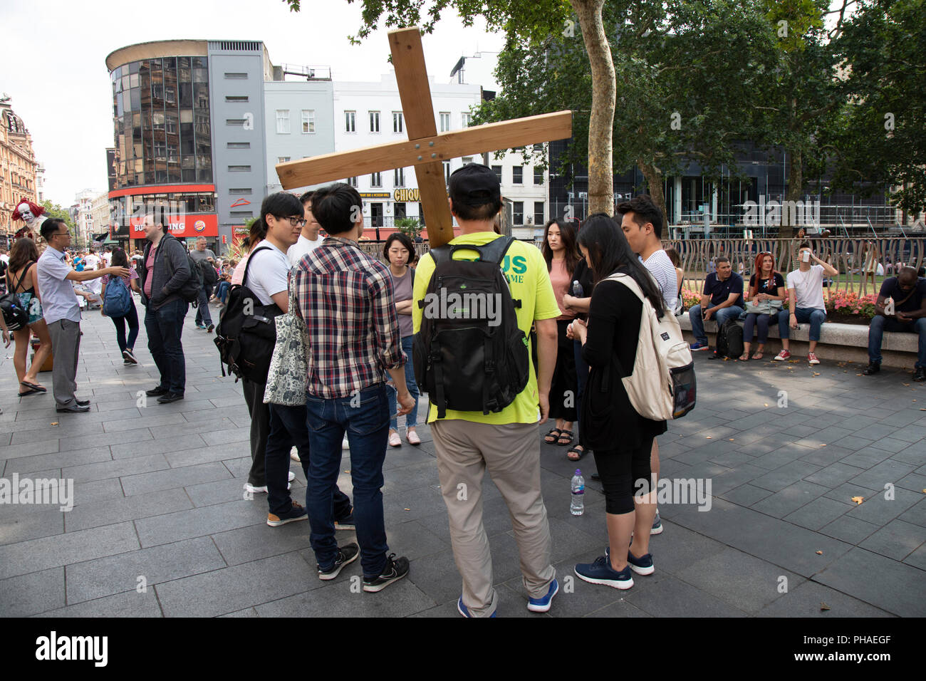 A group of young Koreans in Leicester Square pray and gently spread their faith in Christ and Christianity in London, United Kingdom. Carrying a wooden cross to mark the life of Jesus, they gather in prayer as a very public display of their religion and religious belief. Stock Photo