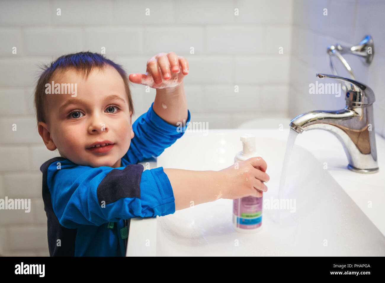Close-up portrait of little white Caucasian boy toddler two years old washing hands in bathroom and looking surprised excited, playing with water and  Stock Photo