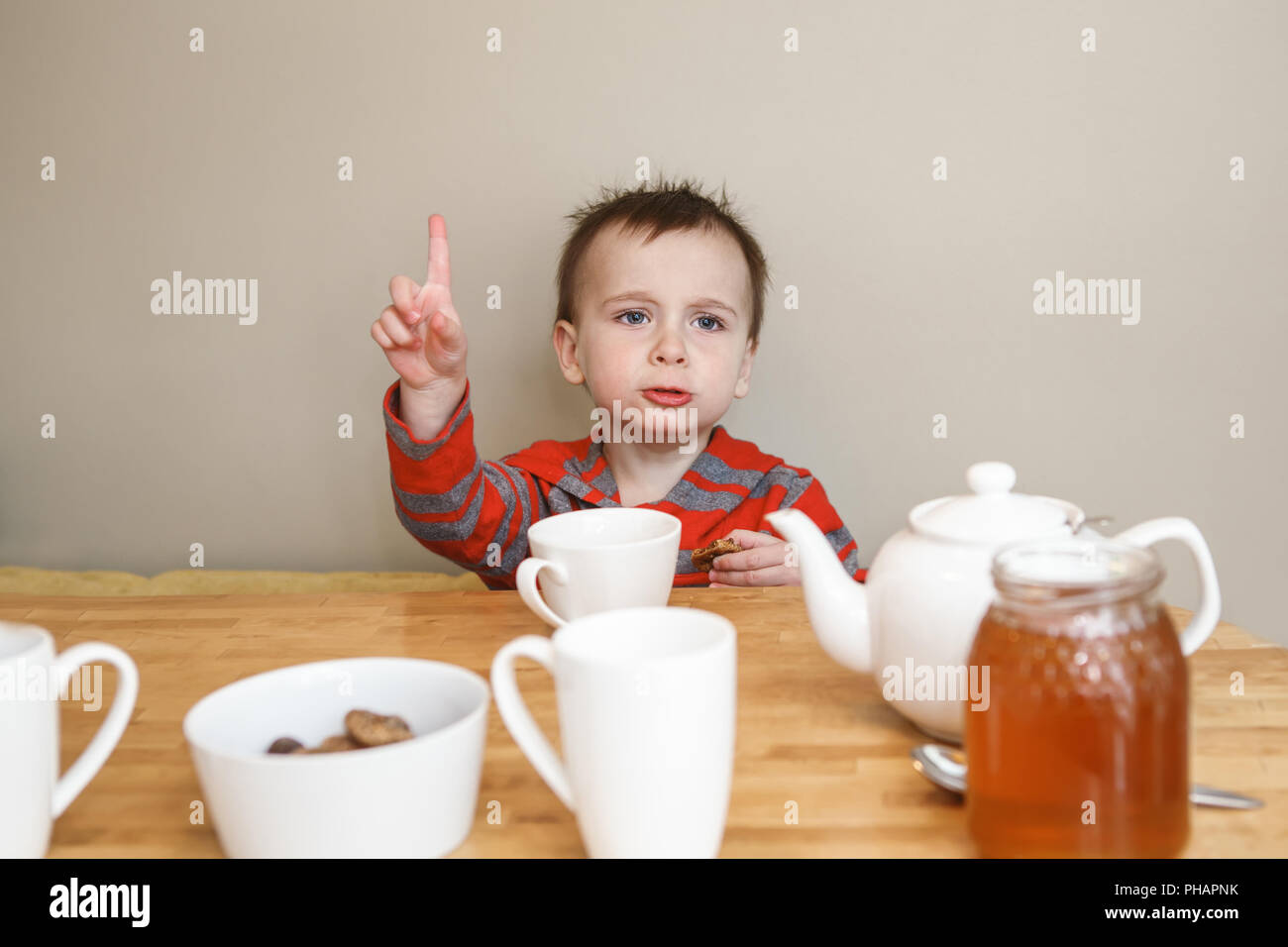 Close-up candid natural portrait of cute little boy toddler in kitchen drinking tea juice, making funny face, showing finger, lifestyle documentary st Stock Photo