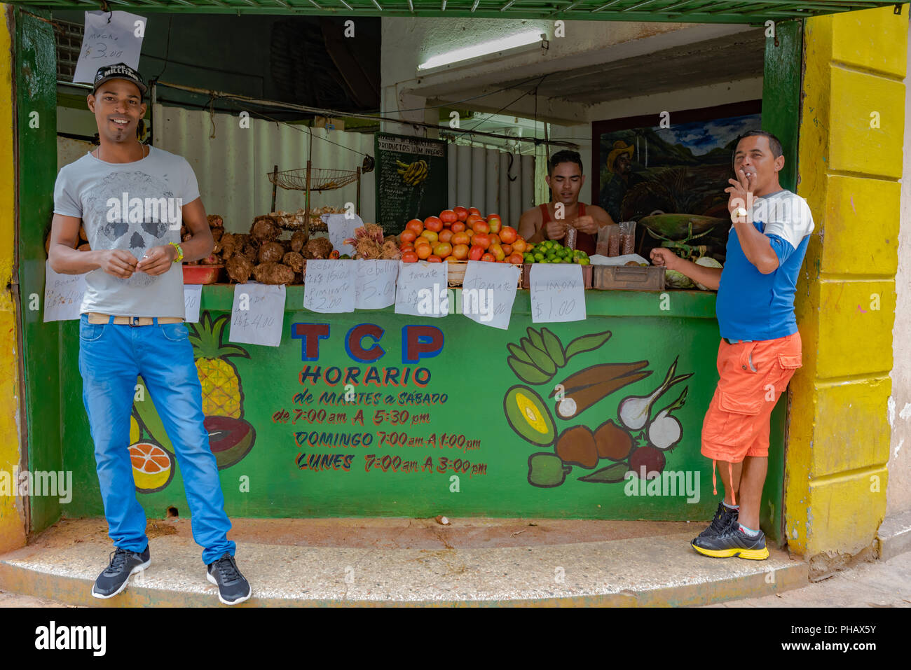 Havana, Cuba / March 21, 2016: Three Cuban men at a fruit stand: one bags nuts, one smokes a cigarette, and the third smiles for the camera. Stock Photo