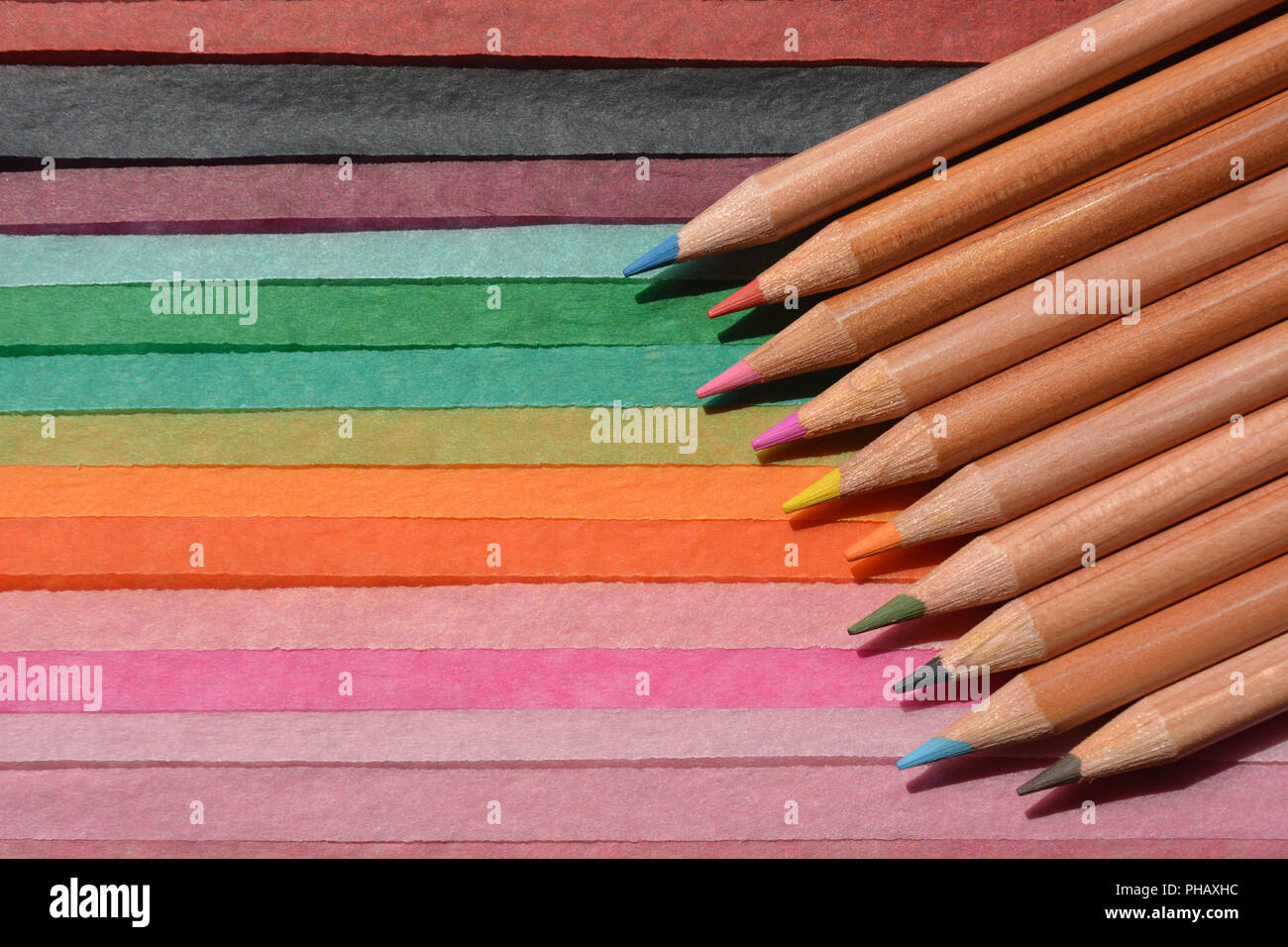 Colour pencils on a brightly coloured, striped,  tissue paper background with copy space. Stock Photo