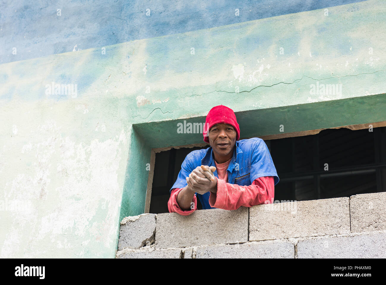 Havana, Cuba / March 22, 2016:  Afro-Cuban laborer, wearing work uniform, looks out window of building under construction. Stock Photo