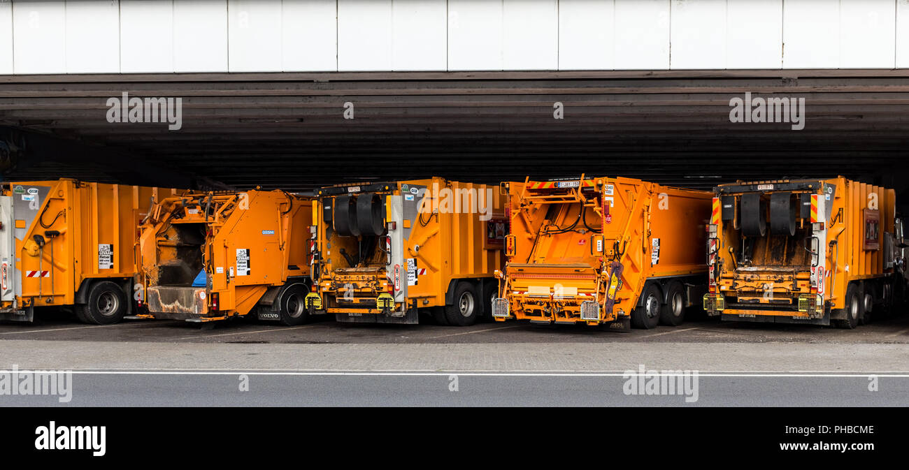 Lineup of orange garbage pickup trucks underneath the viaduct in