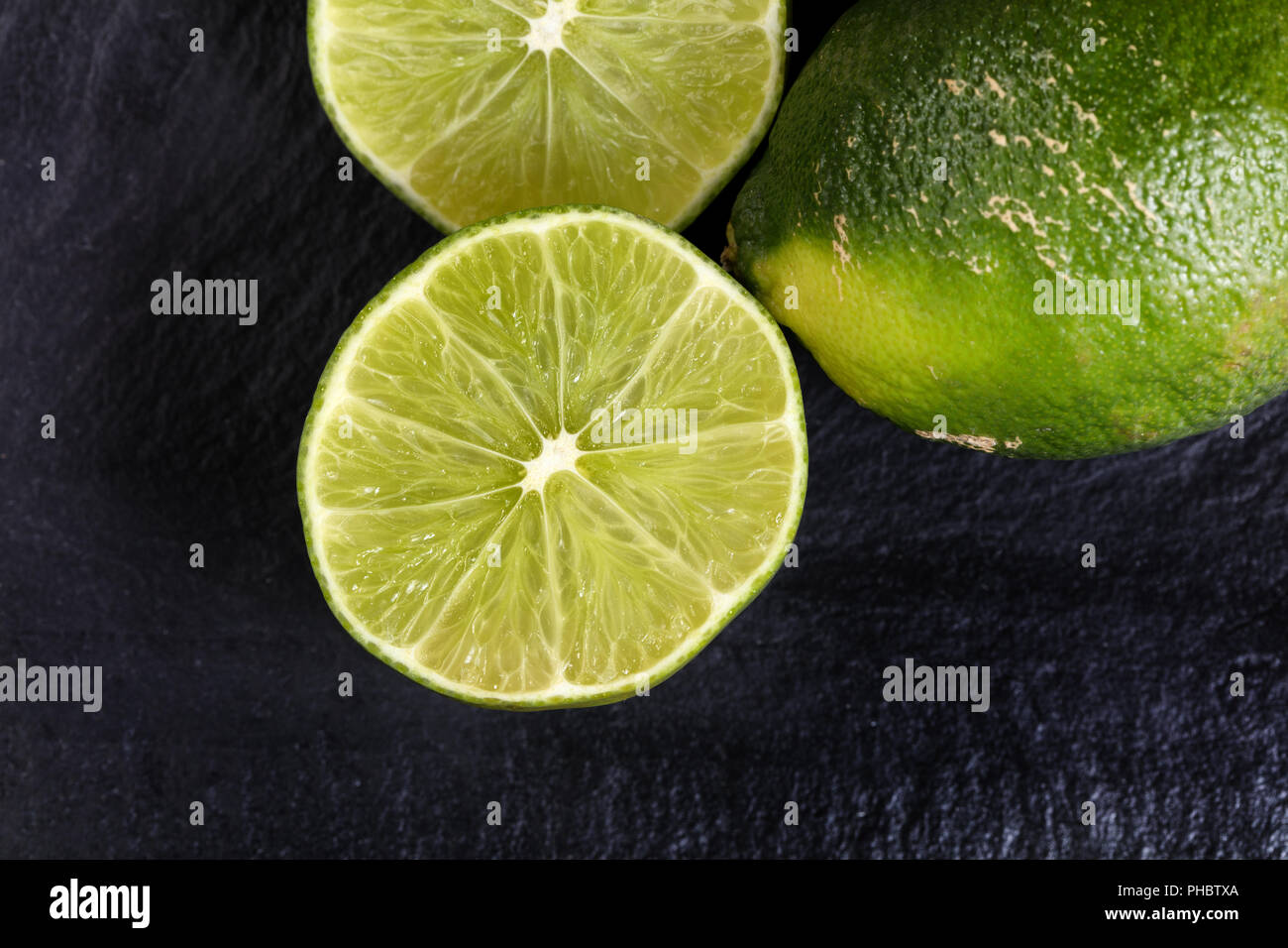 Freshly sliced organic limes on black slate background Stock Photo