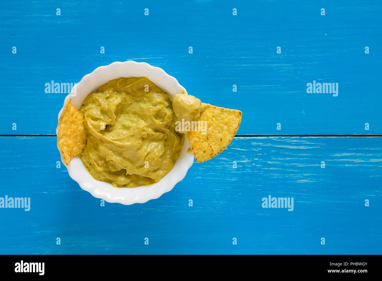 Nachos chips dipping in salsa guacamole over a blue background Stock Photo
