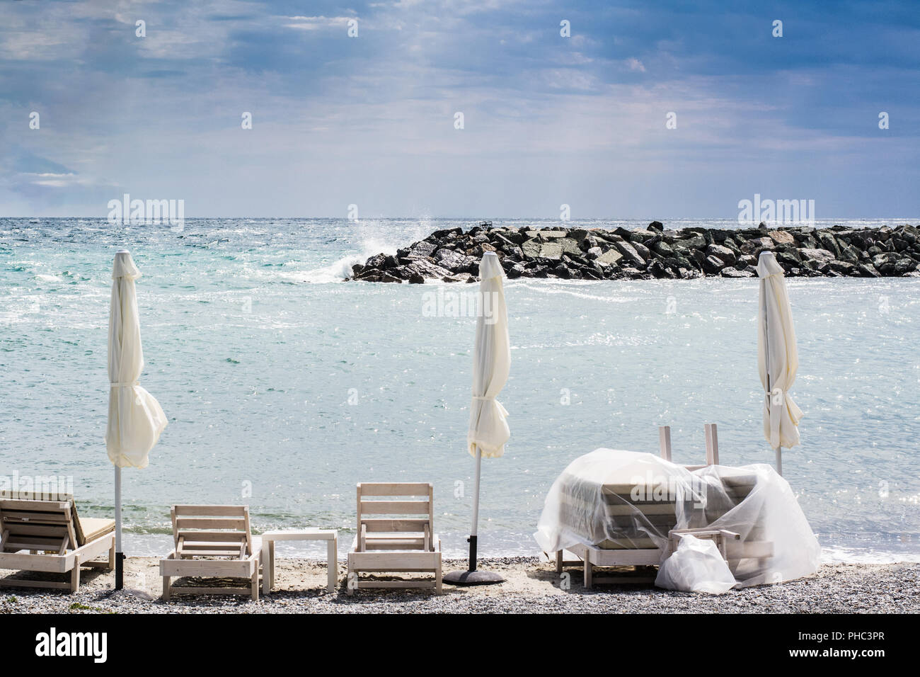 Three Folded umbrellas and chairs on the beach Stock Photo
