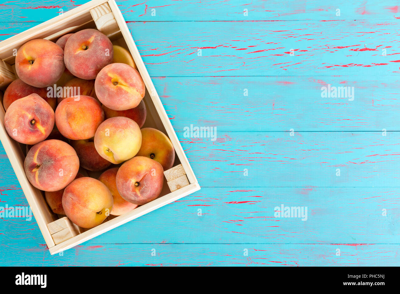 Wooden crate filled with ripe succulent summer peaches placed at an angle on a blue wood background with copy space conceptual of farmers market Stock Photo