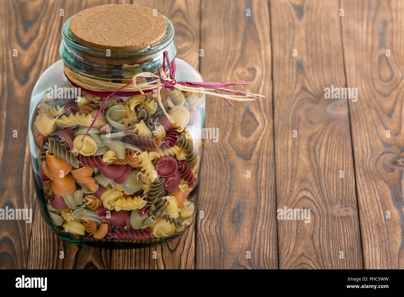 Glass jar of dried fall macaroni pasta in assorted shapes with a cork stopper tied with raffia on a rustic wood background with copy space Stock Photo
