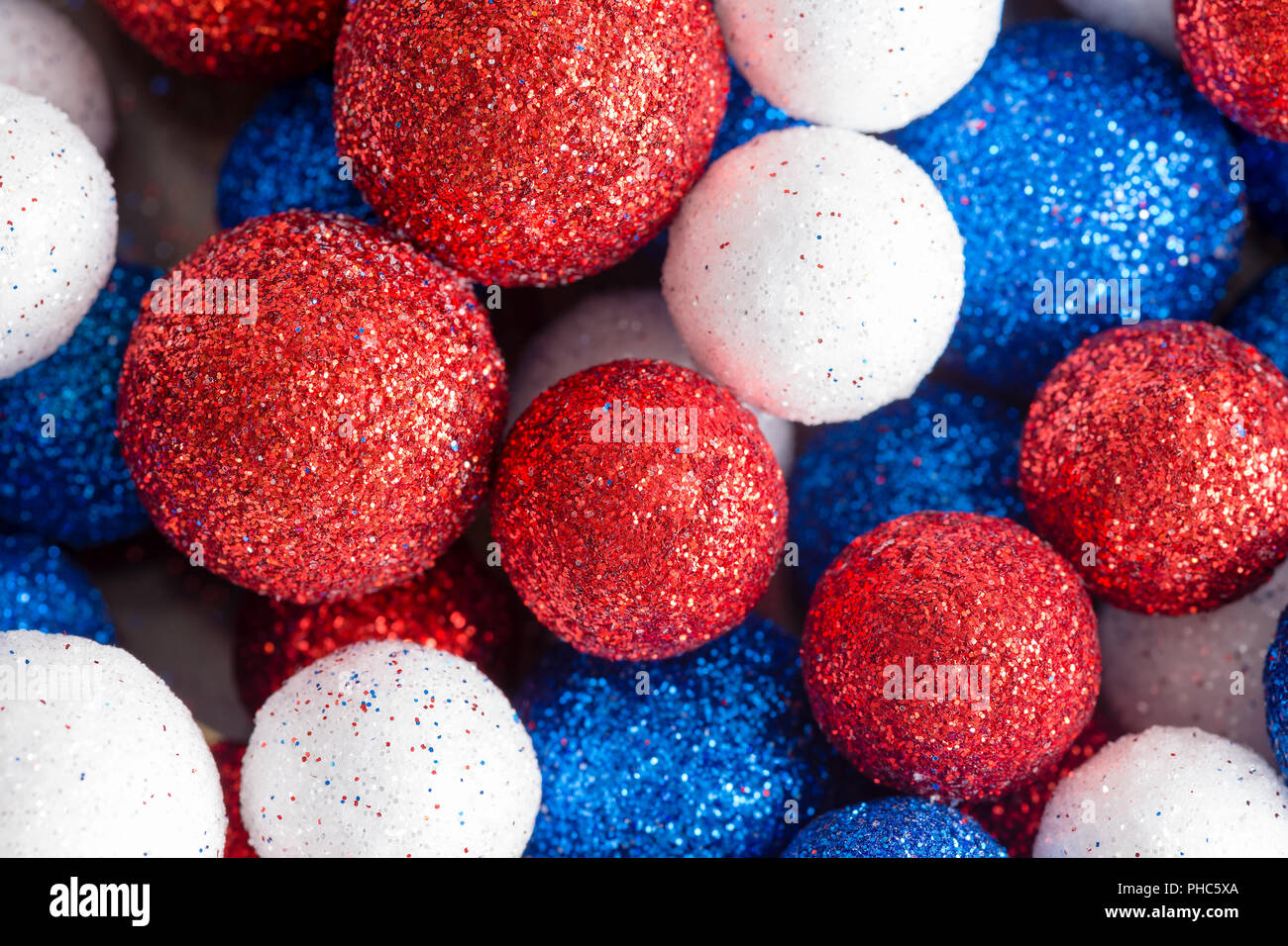 Different sized ornamental red white and blue glitter balls in a random pattern close up full frame view for patriotic American and British themes Stock Photo