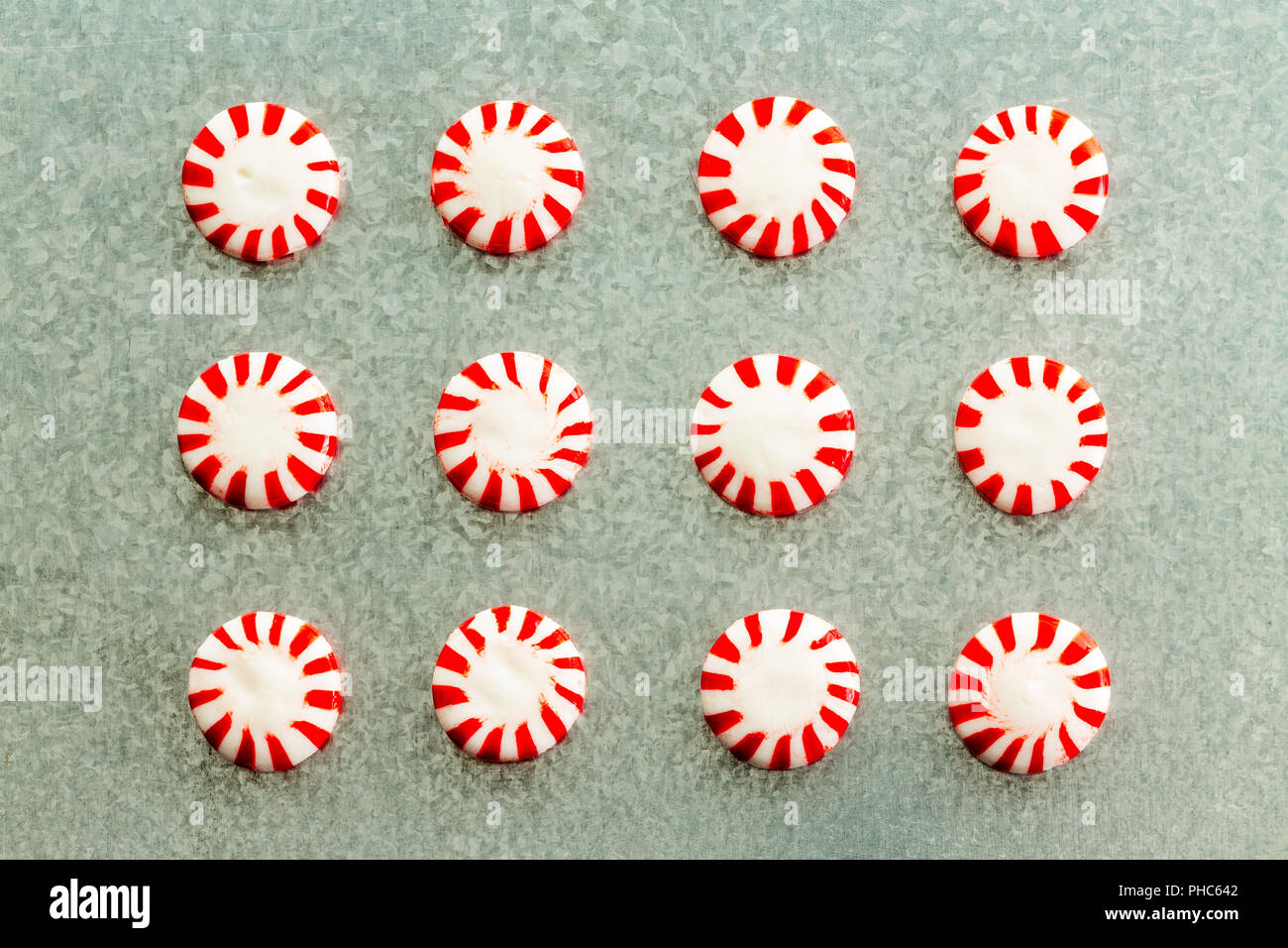 Arrangement of colorful red and white striped peppermint flavored starlight candy in neat rows on a textured grey background viewed from above in a fl Stock Photo