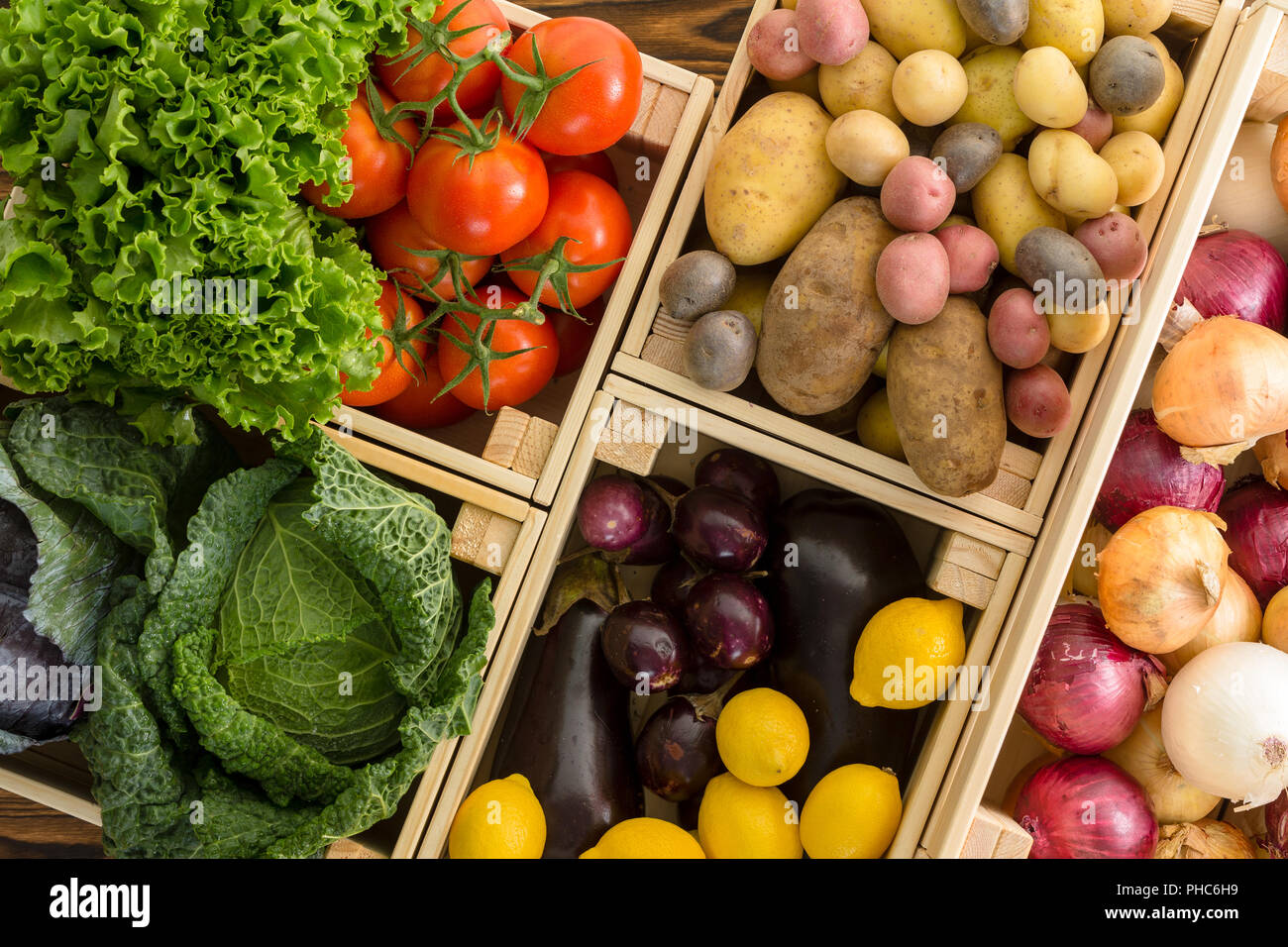 Overhead view on multiple wood crates containing vegetables including potatoes and onions over wooden background Stock Photo