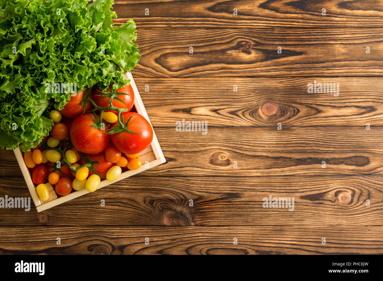 Assortment of ripe whole tomatoes and head of fresh green lettuce in a small wooden box on a table wooden table at an organic farmers market viewed fr Stock Photo