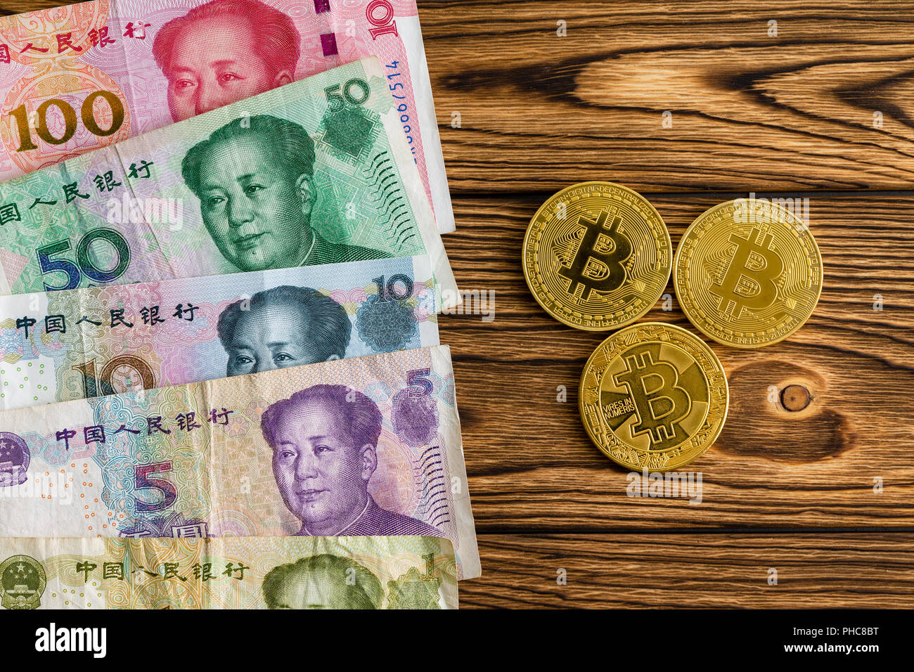 Assorted Chinese Yuan arranged as a border alongside three bitcoins on a wooden table in a comparison between a national currency and virtual digital  Stock Photo