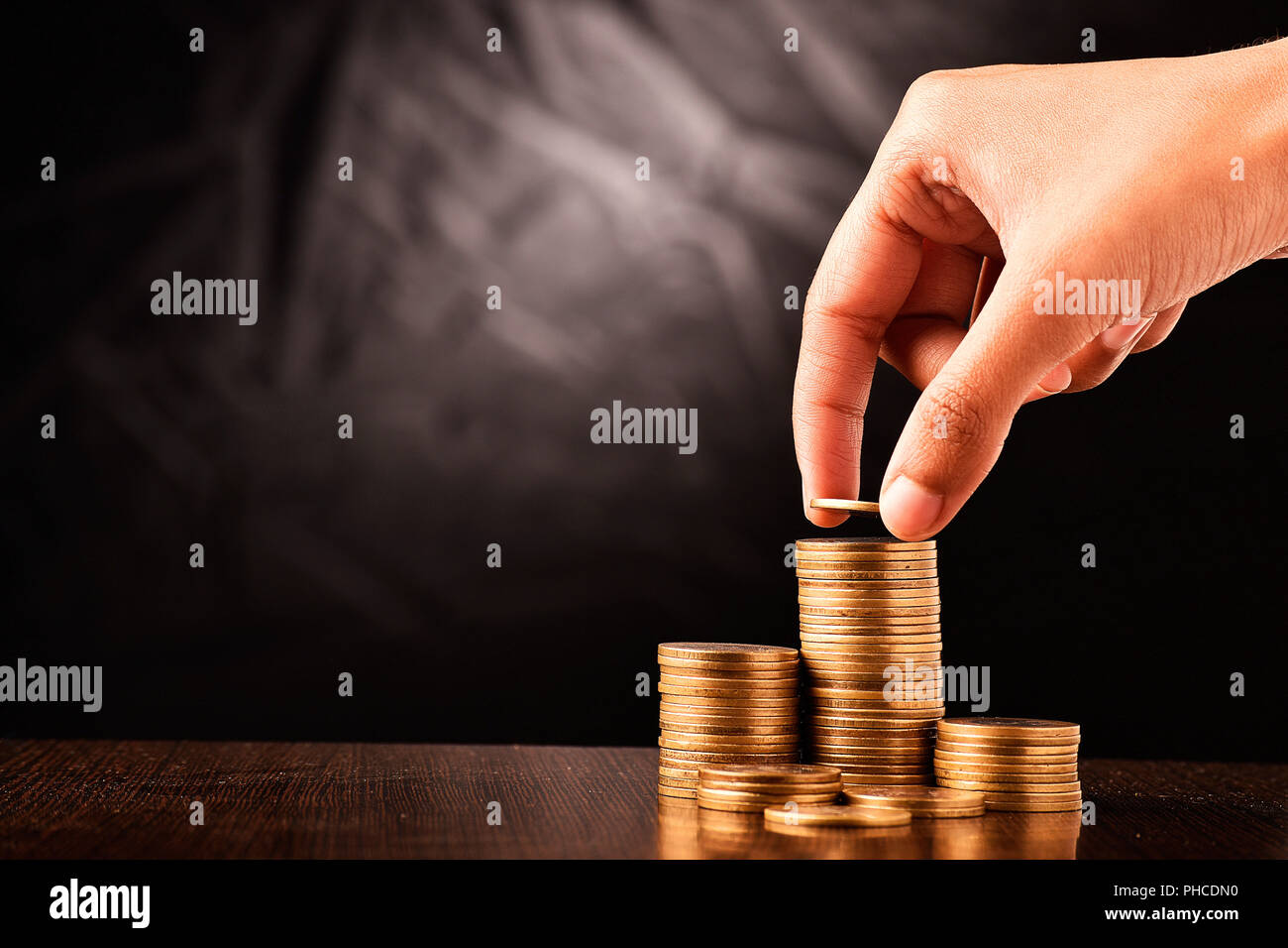 hand putting coins on coins stack sgaint dark background, investment, banking, saving, finance, growth, passive, income, interest, salary concept. Stock Photo