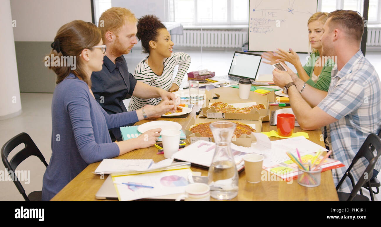 Colleagues eating pizza at office table Stock Photo