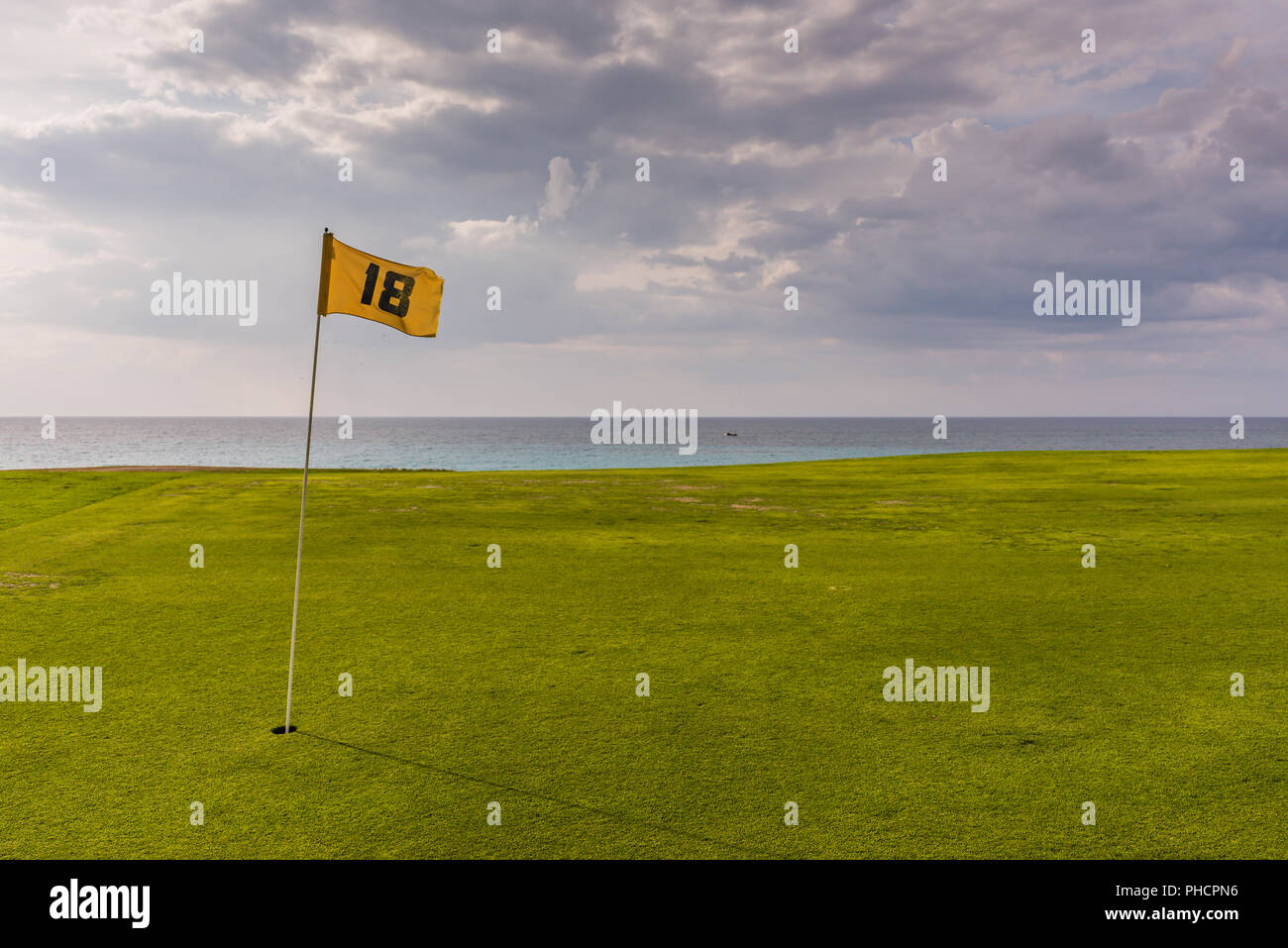 Varadero, Cuba / March 19, 2016: Yellow flag on smooth green lawn by the ocean at Cuban golf club. Stock Photo