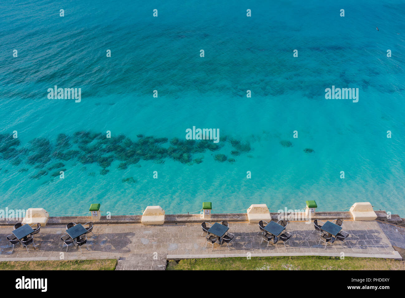 Row of bistro tables on patio by translucent turquoise ocean in Varadero, Cuba. Stock Photo