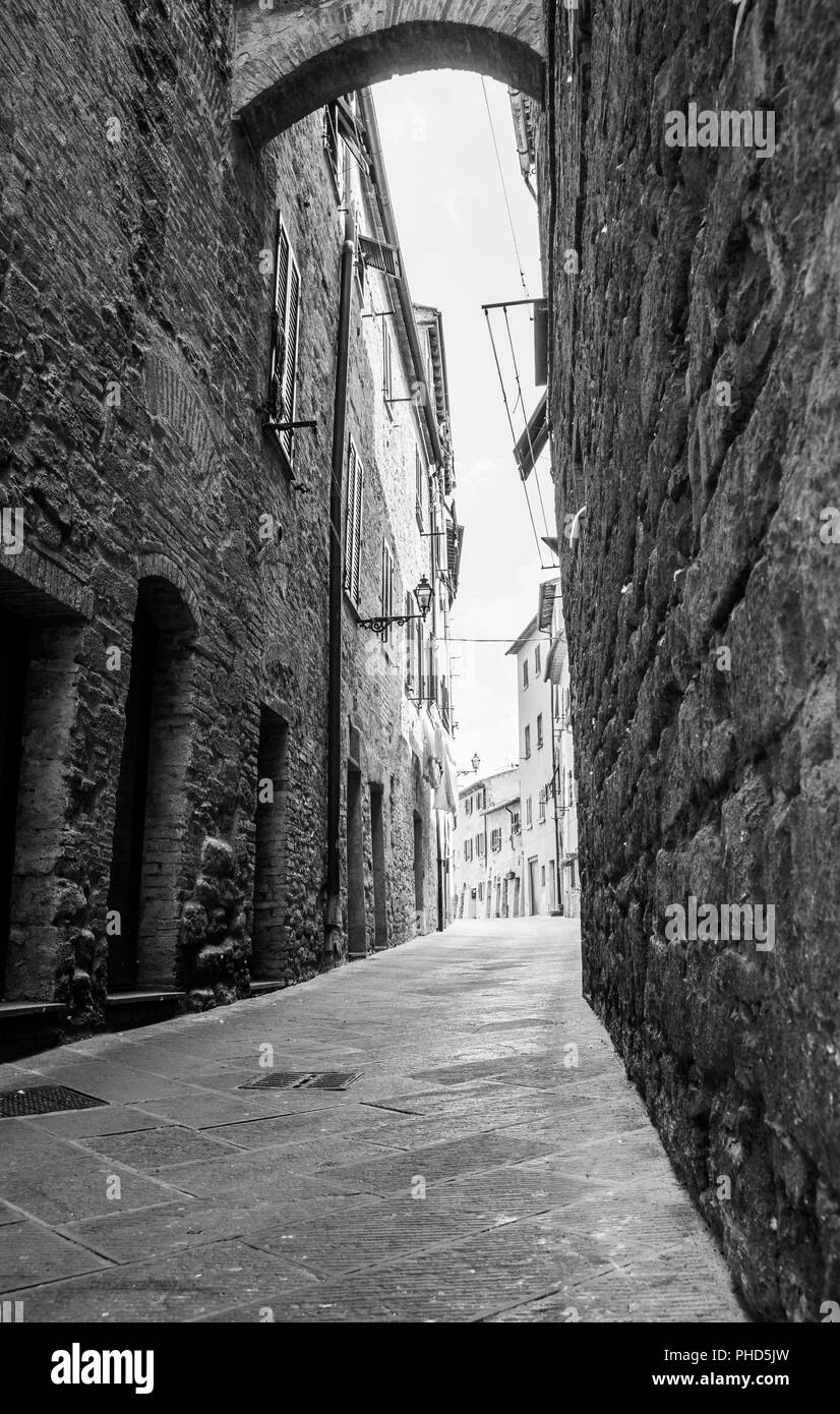 Rough stone walls in dark narrow laneway lined by high stone buildings leading bright street ahead. Stock Photo