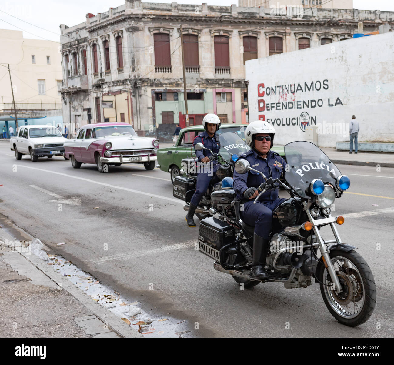 Two motorcycles carrying Cuban police in the foreground while in the background a mural about revolution. Stock Photo