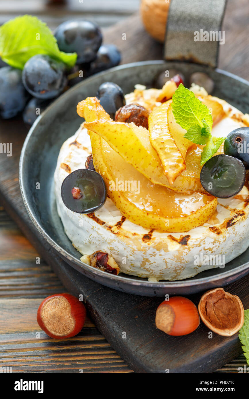 Camembert baked with pear and black grapes. Stock Photo
