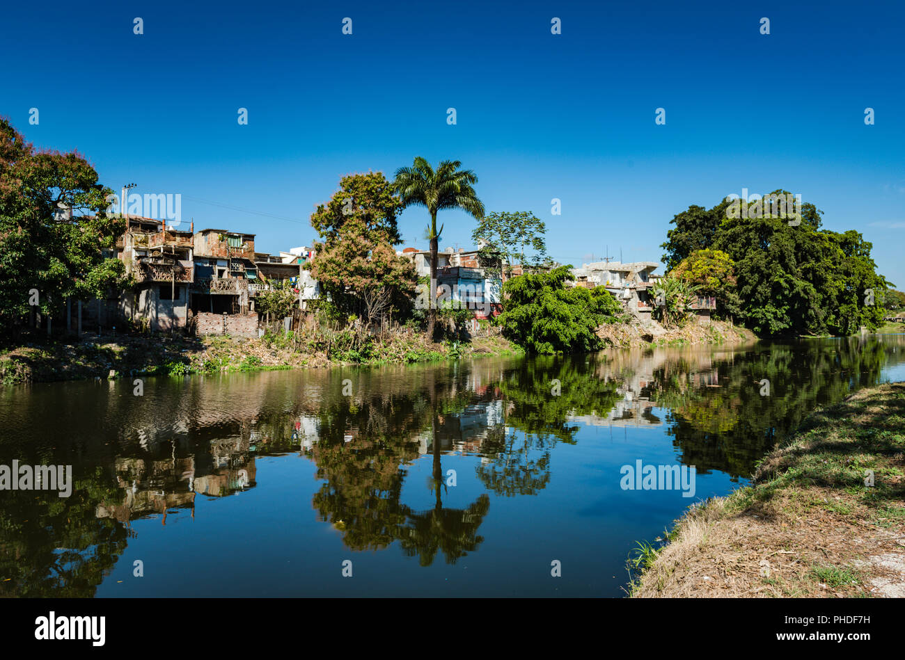 Calm reflections on Yayabo River with view of apartment housing in Sancti  Spiritus , Cuba. Stock Photo