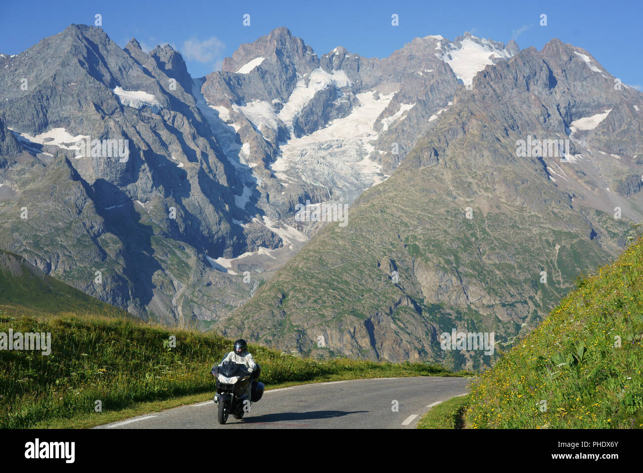 Motorcyclist cruising with the lofty peaks and glaciers of the Écrins Massif in the background. Between Col du Lautaret and Col du Galibier, France. Stock Photo