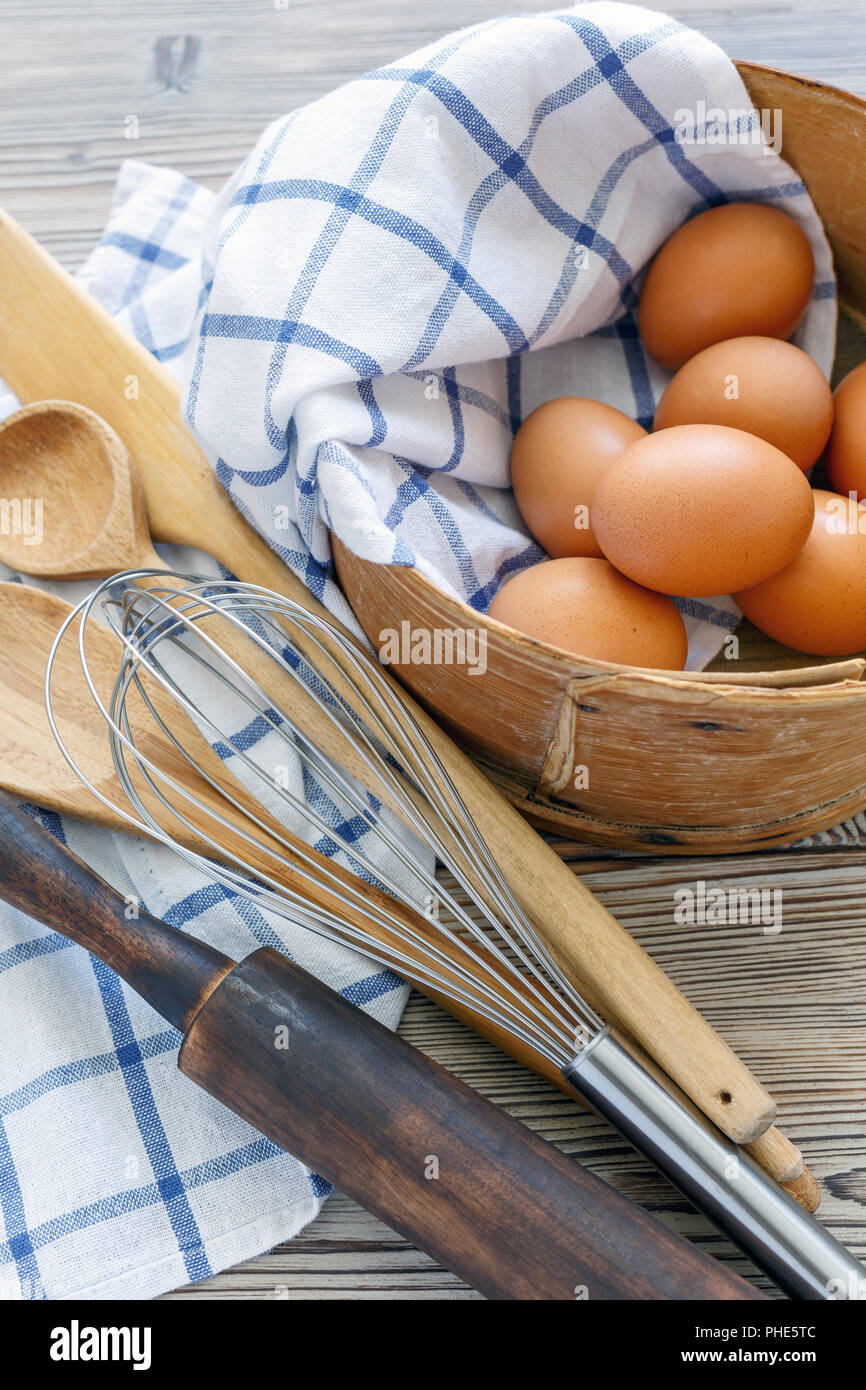 Brown eggs in old sieve,rolling pin,whisk and spoon. Stock Photo