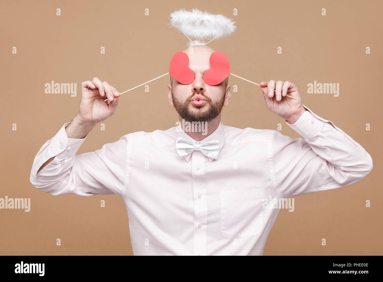 Happy handsome middle aged bald bearded angel in shirt and white halo on head standing and closing the eyes with two heart stickers and air kissing. s Stock Photo