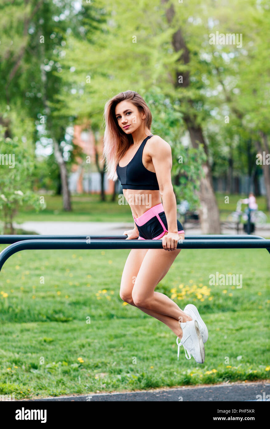 Woman pull-ups herself up on bar on sports ground in park. Stock Photo