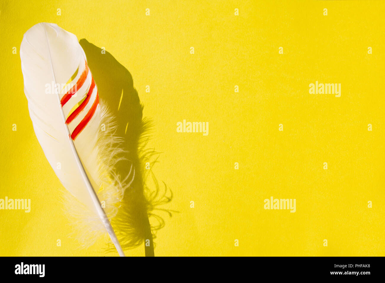 feather on a yellow background Stock Photo - Alamy