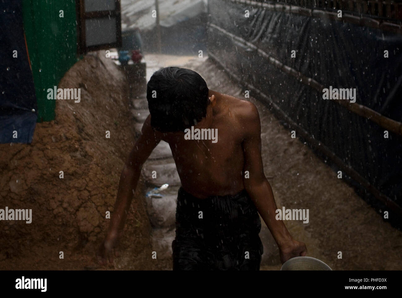 A boy collects water during heavy rain in Chakmakul, one of the camps sheltering over 800,000 Rohingya refugees, Cox's Bazar, Bangladesh, July 4, 2018 Stock Photo