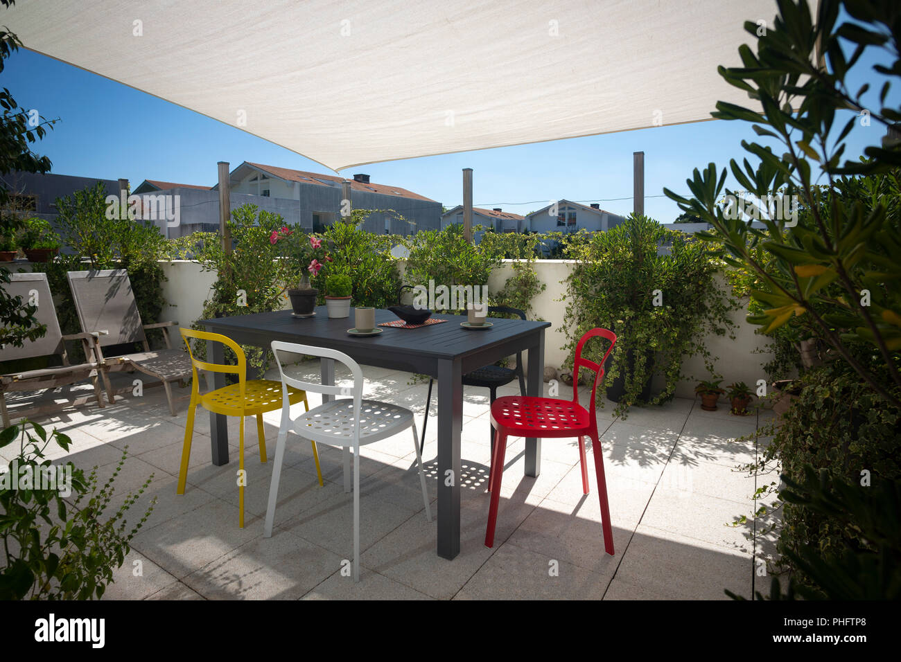 The terrace of a flat furnished with a set of garden furniture, deck chairs and a sun shade sail. Stock Photo