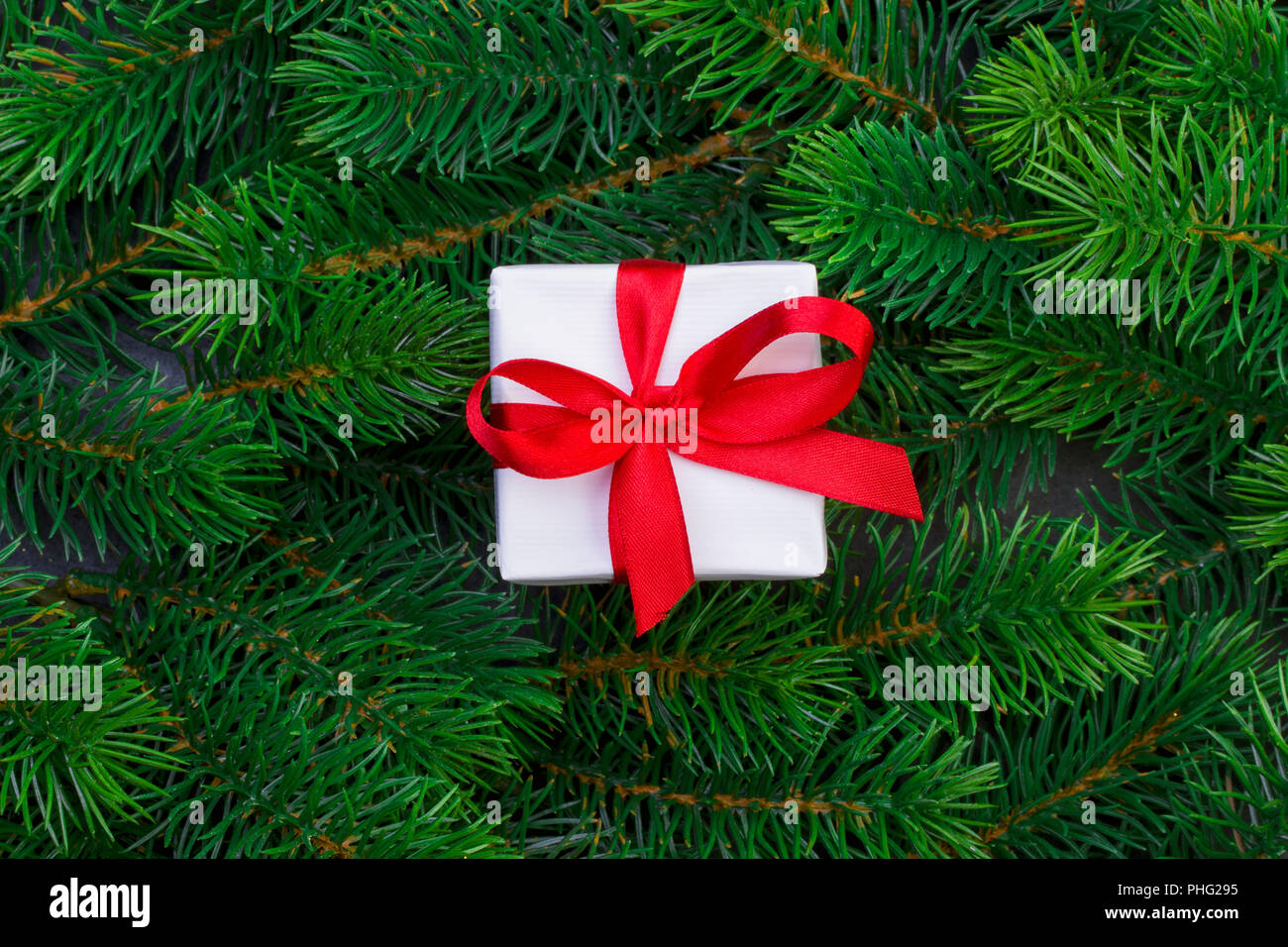 Gift box with red ribbon on the background of christmas tree branches ...