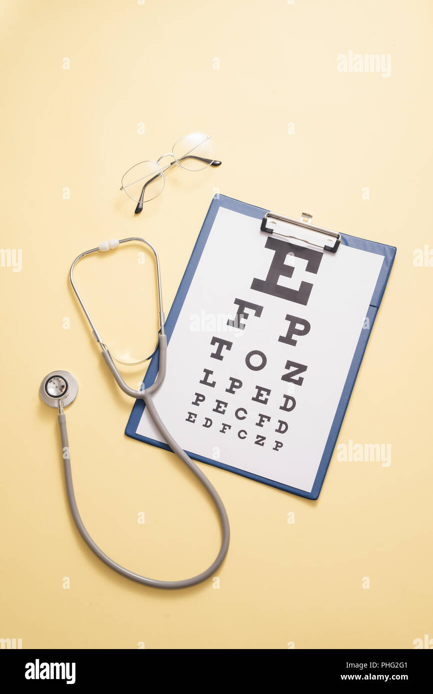 Table for visual acuity test and medical stethoscope is in yellow background. Concept of eye diagnosis, detection of eye diseases in opthalmology Stock Photo