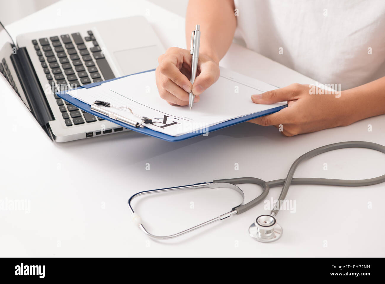 Doctor hand hold silver pen filling patient history list at clipboard