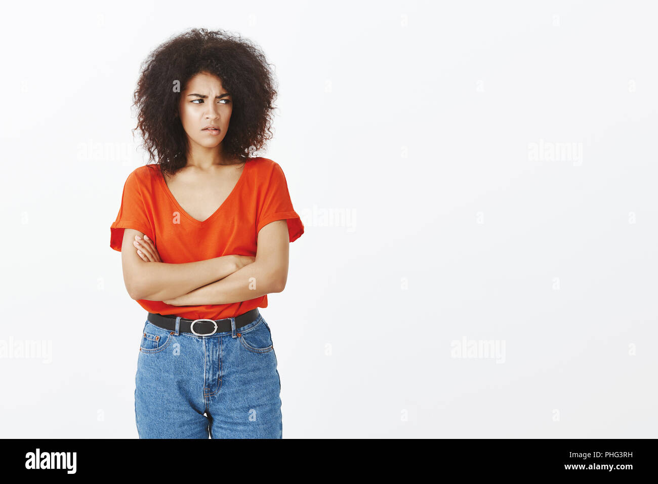 Indoor shot of attractive female social outcast with afro hairstyle, frowning, holding hands crossed on chest, staring with offence right, being offended or insulted over gray background Stock Photo