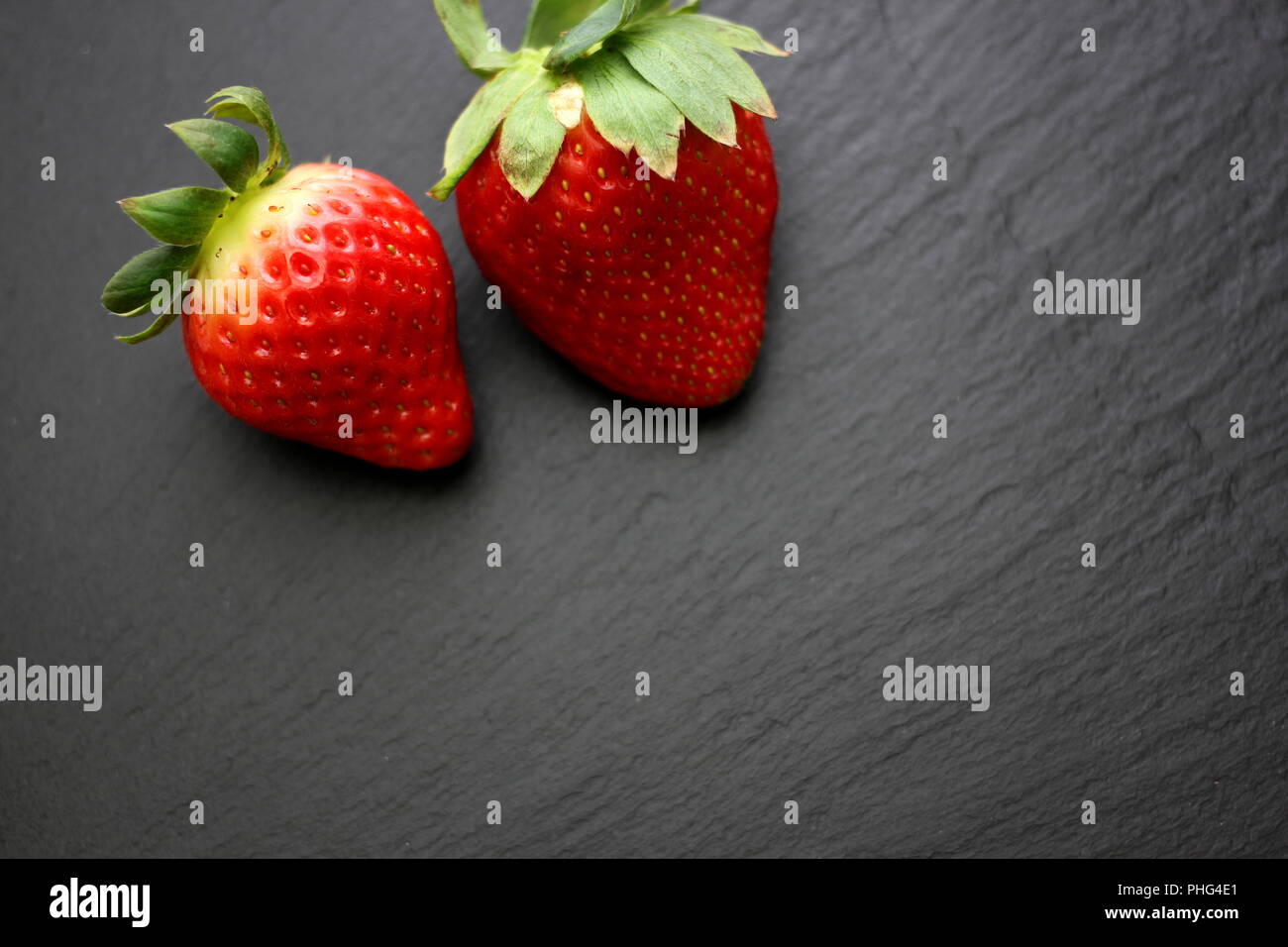 Two strawberries on black slate plate Stock Photo
