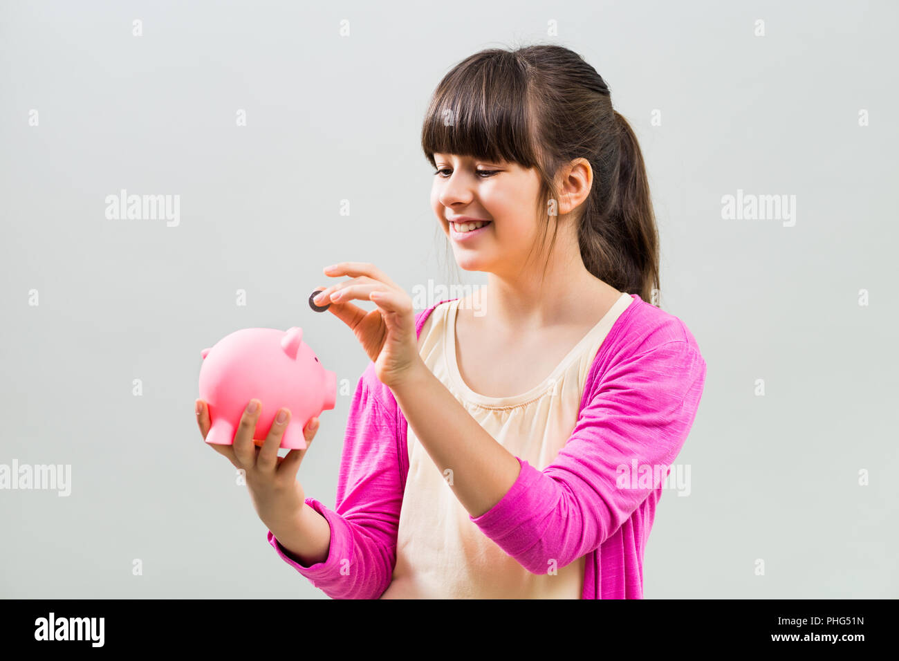 Cute little girl putting coin into piggy bank Stock Photo - Alamy