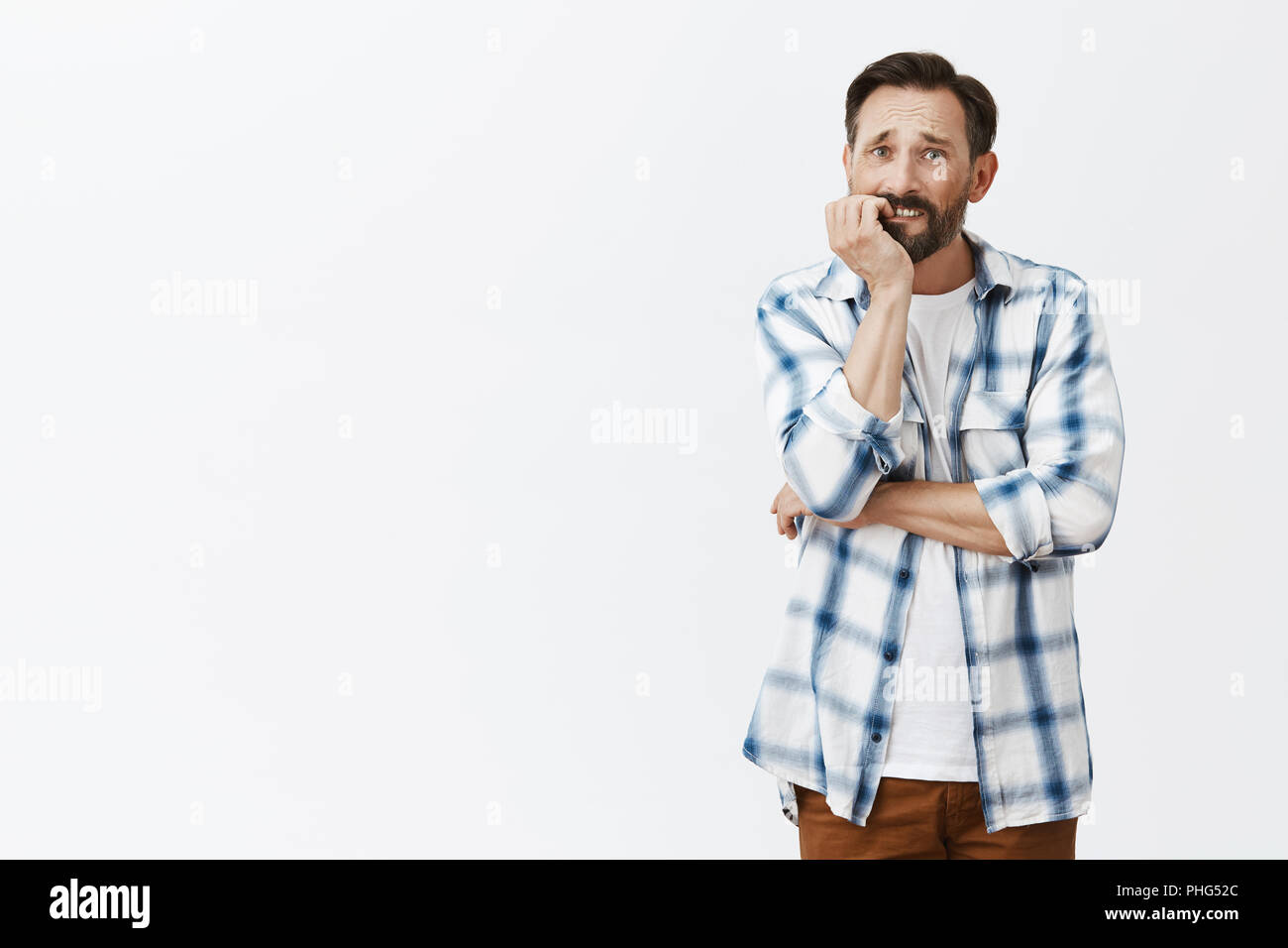 Man trying quiet smoking, biting fingernails while feeling need to smoke, frowning and gazing with sad expression aside, thinking, trying to control feelings, standing over gray background anxious Stock Photo