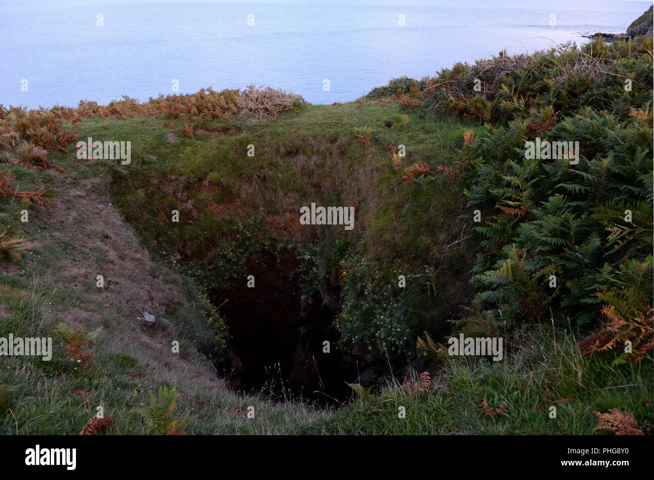 Blow hole with sea cave entrance at base. Wave action has exploited weaknesses in the rock  to form this vertical shaft. Stock Photo