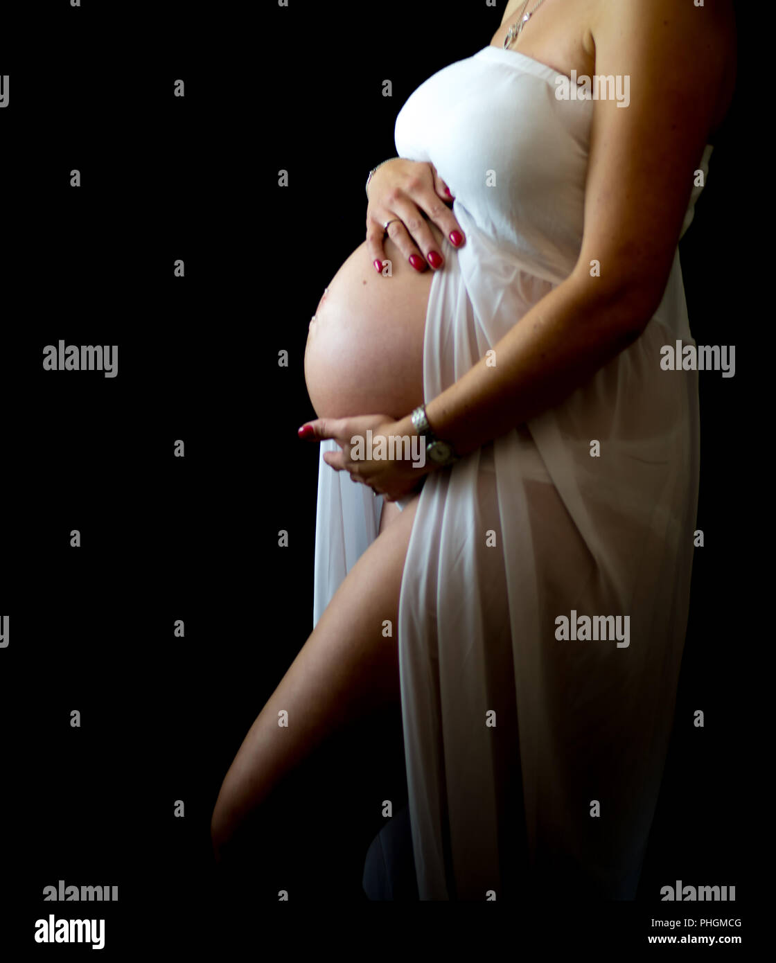 3/4 length side proflie of pregnant lady cradling her baby bump with black back ground Stock Photo