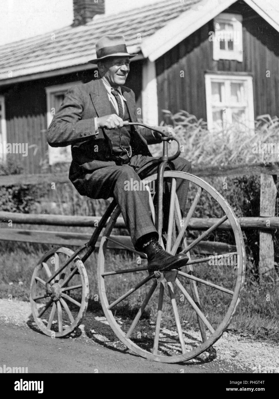 Penny farthing bicycle. A man is riding a penny-farthing bicycle he has made himself with wooden wheels both front and back. Sweden 1940s Stock Photo