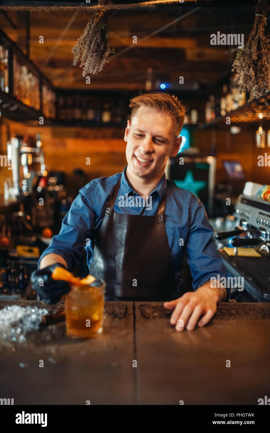 Male bartender in apron works at the bar counter. Alcohol beverage preparation. Barman occupation, barkeeper job Stock Photo